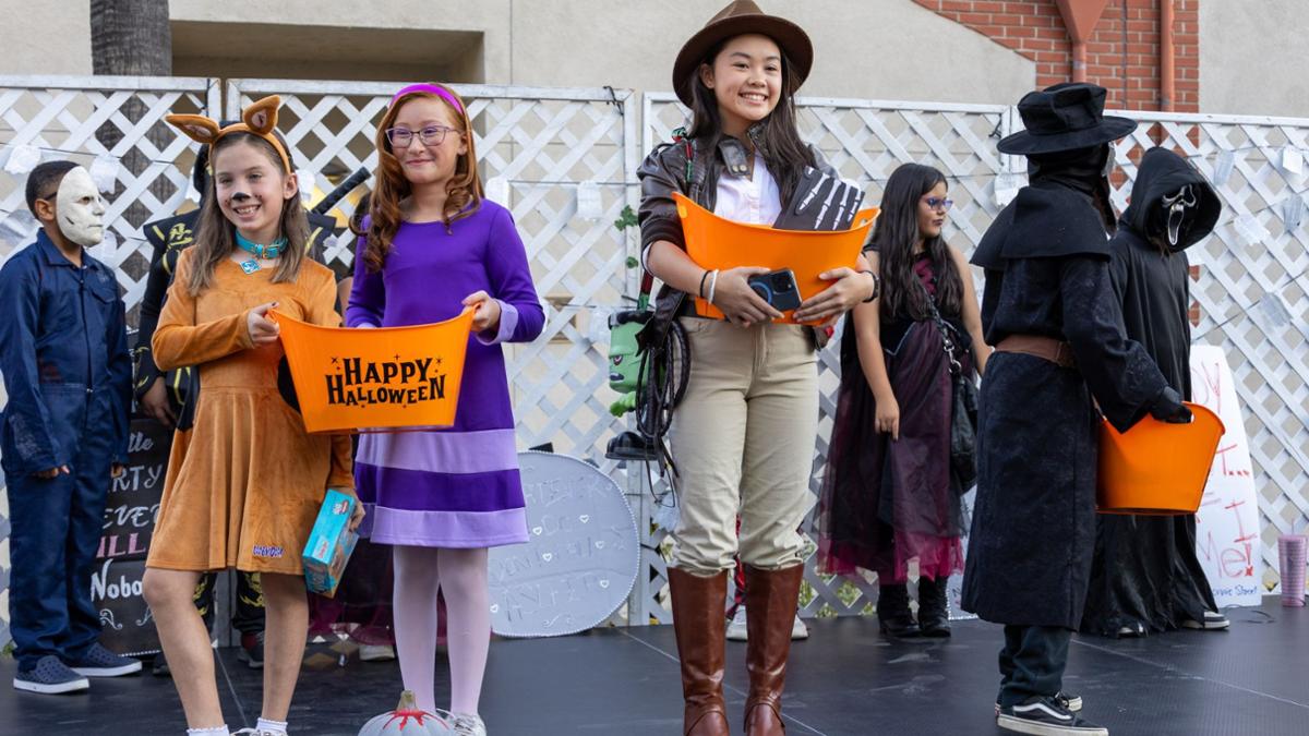 Winners in a costume contest holding prize buckets that say happy halloween - one dressed as an archeologist adventurer, scooby doo and Daphne